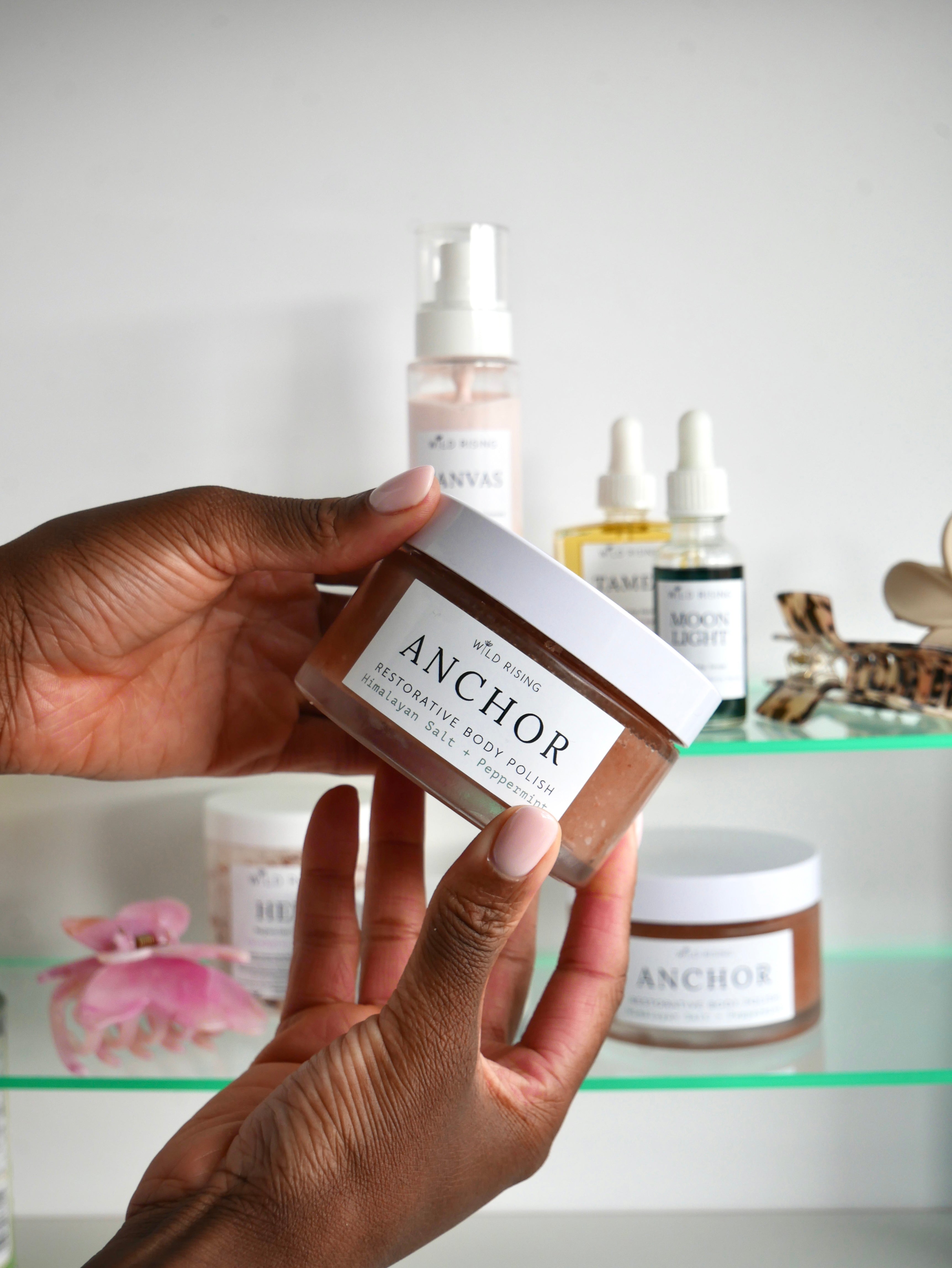 Hand holding a jar of Anchor body butter with skincare products in the background.