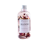 A clear bottle of Wild Rising Bloom nourishing body oil with dried rose petals suspended inside, set against a plain white background.
