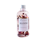 A clear bottle of Wild Rising Bloom nourishing body oil with dried rose petals suspended inside, set against a plain white background.