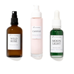 Three skincare products from WILD RISING on a white background: an amber spray bottle labeled Wild Rose, a pale pink pump bottle labeled Canvas, and a green dropper bottle labeled Moon Light.