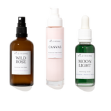 Three skincare products from WILD RISING on a white background: an amber spray bottle labeled Wild Rose, a pale pink pump bottle labeled Canvas, and a green dropper bottle labeled Moon Light.