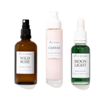 Three skincare products from WILD RISING on a white background: an amber spray bottle labeled Wild Rose, a pale pink pump bottle labeled Canvas, and a green dropper bottle labeled Moon Light.