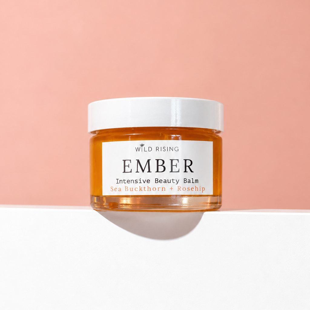 A jar of Wild Rising Ember Intensive Beauty Balm with amber-colored balm visible through a clear jar and a white lid, set against a split peach and white background.