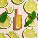 Skincare bottle labeled 'Wild Rising' surrounded by lime slices and mint leaves on a beige background