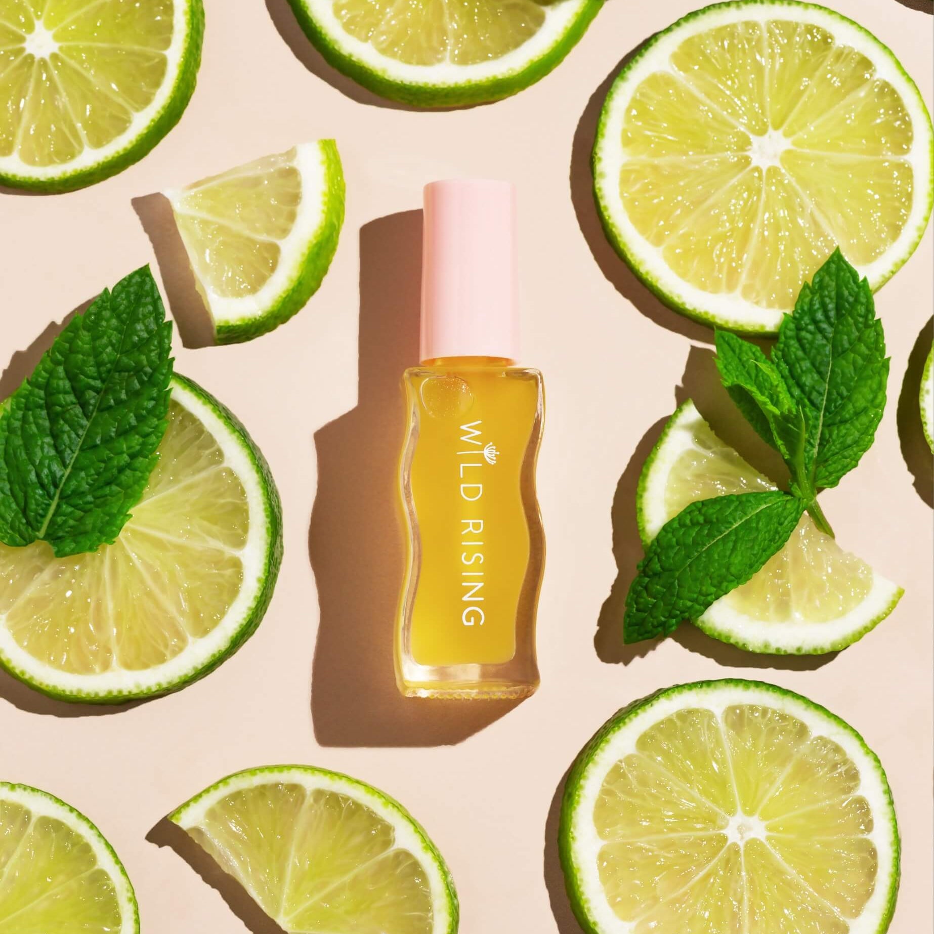 Skincare bottle labeled 'Wild Rising' surrounded by lime slices and mint leaves on a beige background