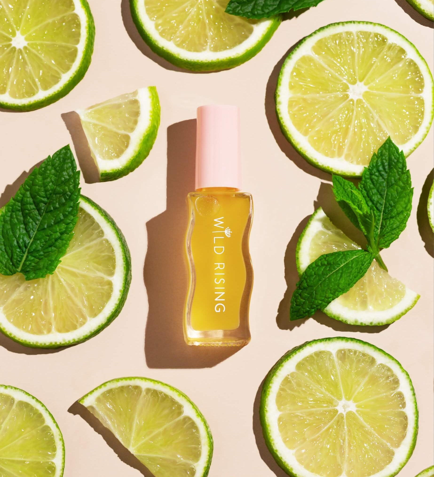 Skincare bottle labeled 'Wild Rising' surrounded by lime slices and mint leaves on a beige background