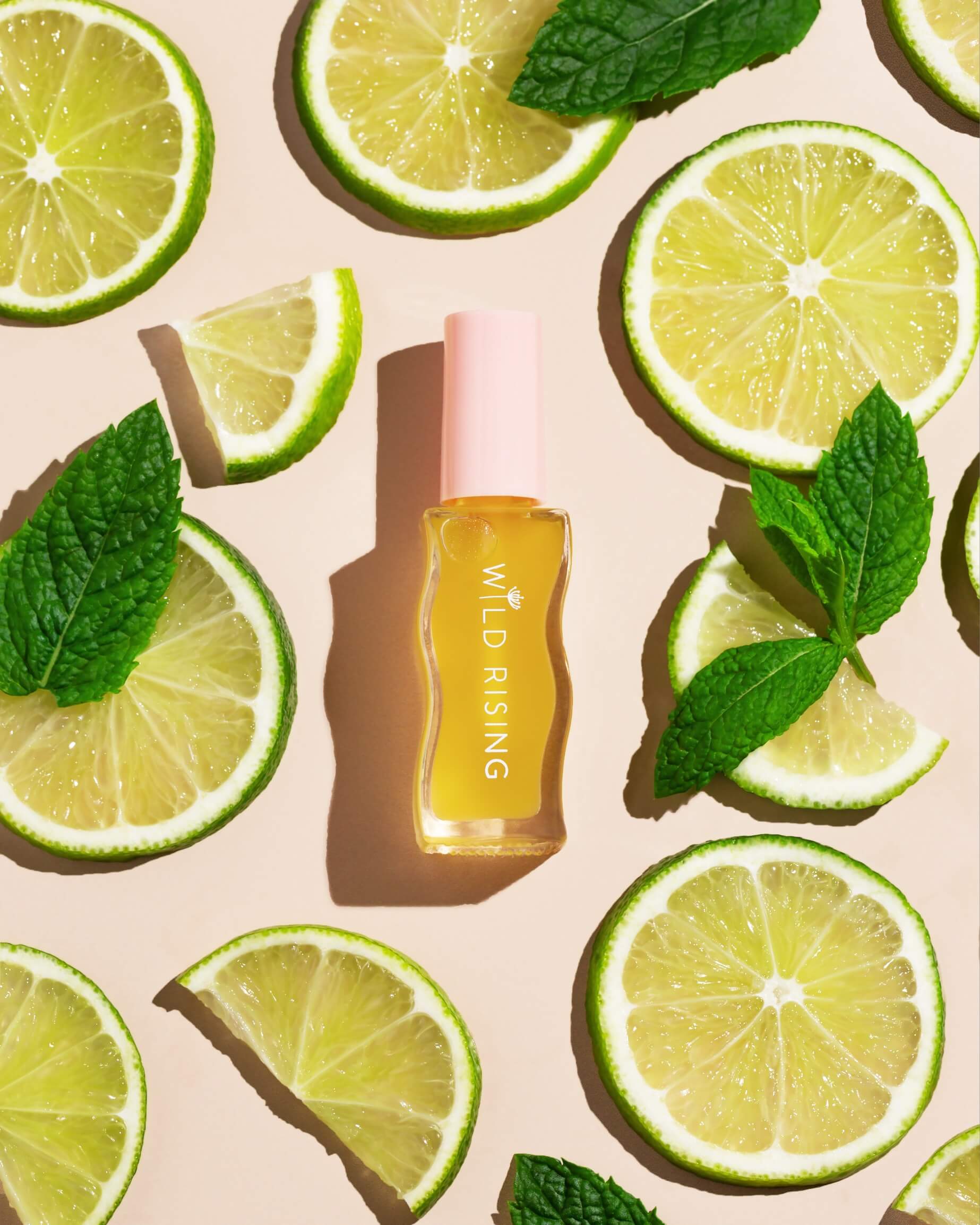 Skincare bottle labeled 'Wild Rising' surrounded by lime slices and mint leaves on a beige background