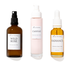 Three skincare products from Wild Rising on a white background: Wild Rose Balancing Face Toner in an amber spray bottle, Canvas Moisturising Cream Cleanser in a pale pink pump bottle, and Radiance Serum in an amber dropper bottle.