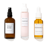 Three skincare products from Wild Rising on a white background: Wild Rose Balancing Face Toner in an amber spray bottle, Canvas Moisturising Cream Cleanser in a pale pink pump bottle, and Radiance Serum in an amber dropper bottle.