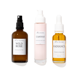Three skincare products from Wild Rising on a white background: Wild Rose Balancing Face Toner in an amber spray bottle, Canvas Moisturising Cream Cleanser in a pale pink pump bottle, and Radiance Serum in an amber dropper bottle.