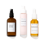 Three Wild Rising skincare bottles on a white background: an amber spray bottle labeled Wild Rose, a pale pink pump bottle labeled Canvas, and an amber dropper bottle labeled Radiance.