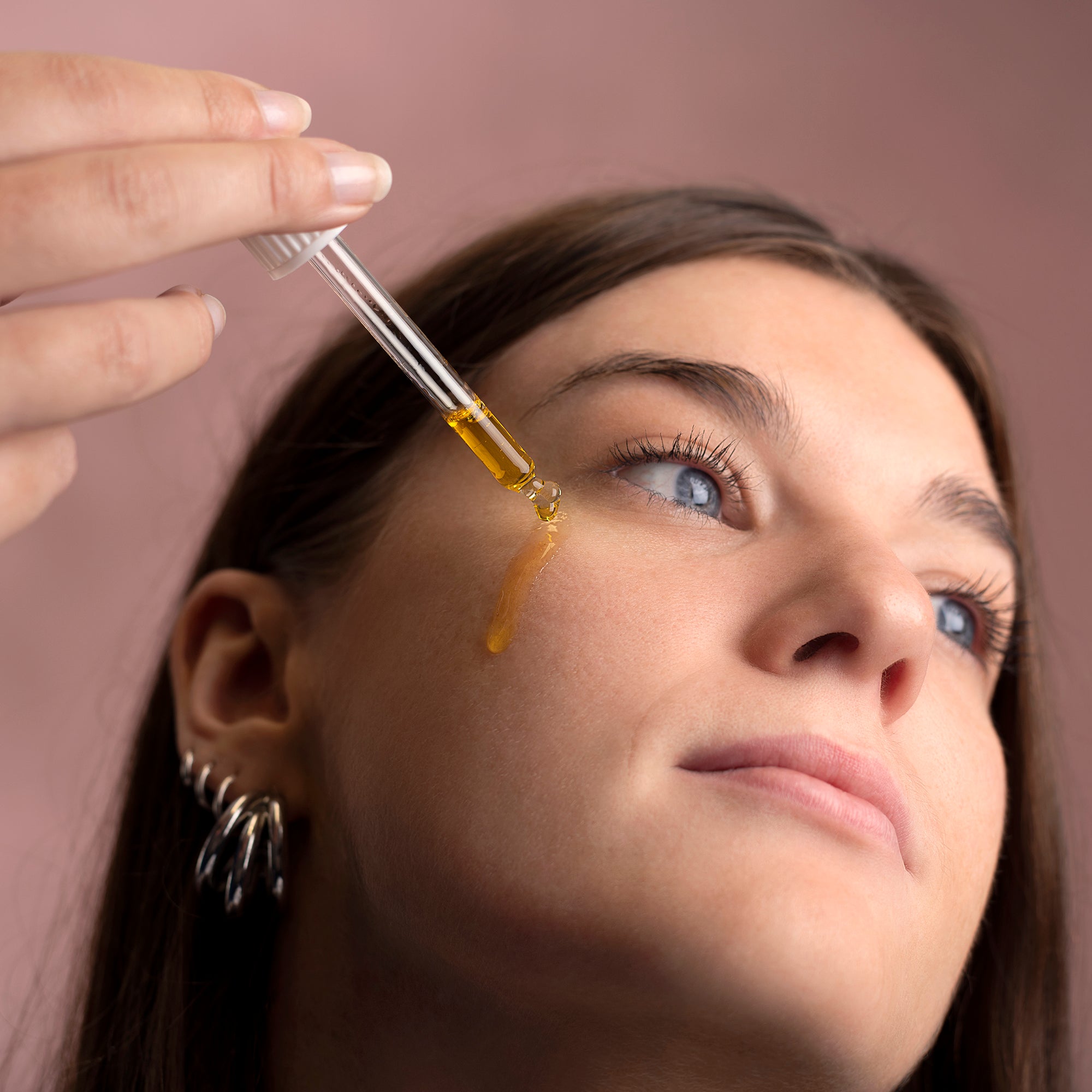 Person applying a dropper of liquid to their eye with a brown background