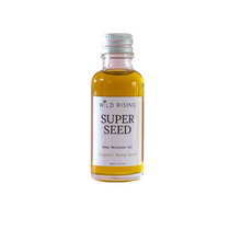A small glass bottle of Wild Rising Super Seed Deep Moisture Oil filled with golden-yellow oil, featuring a white label and a silver metal cap, set against a plain white background.