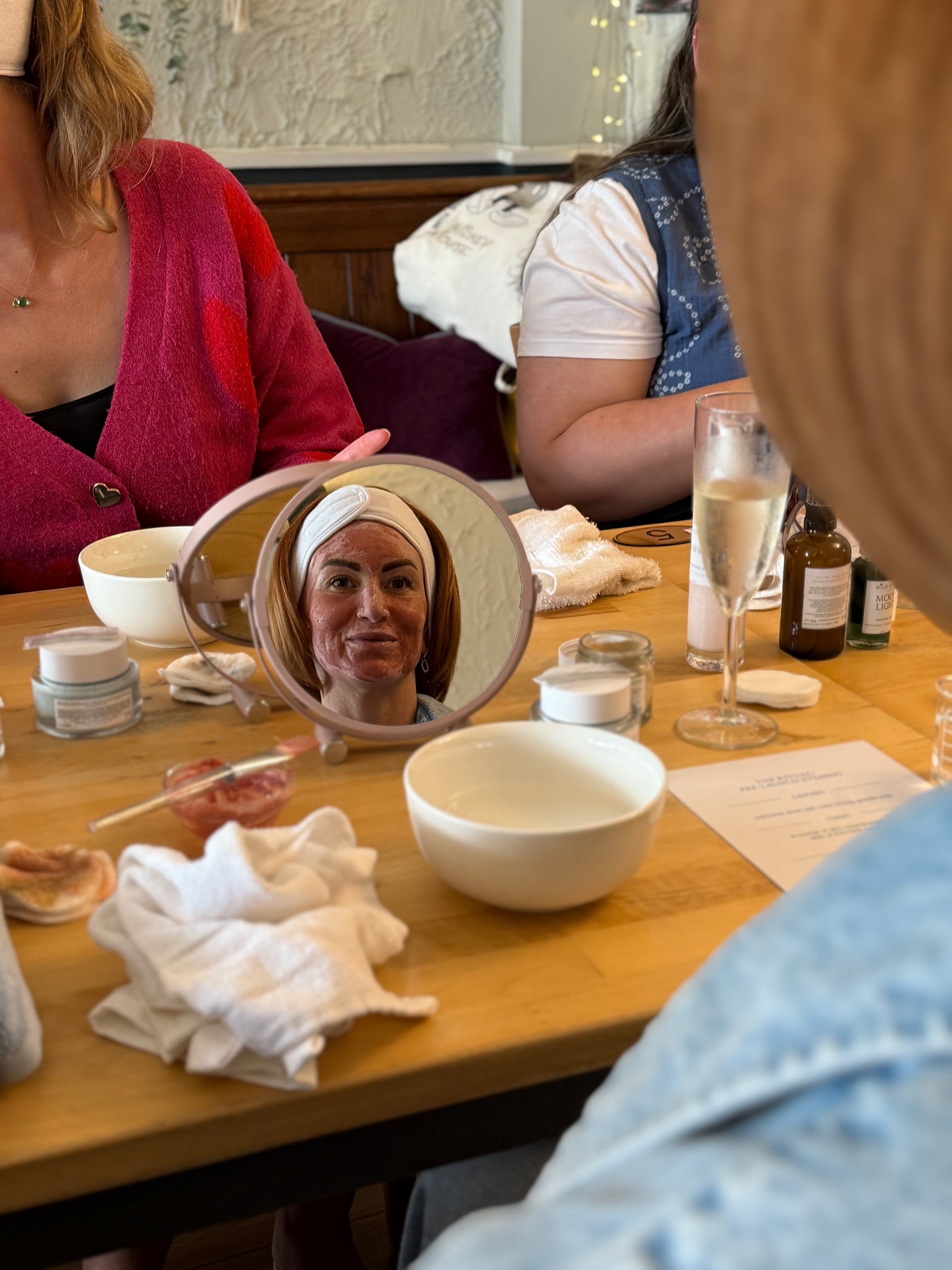 Woman looking into a small mirror at a table with various items including a bowl and a bottle.