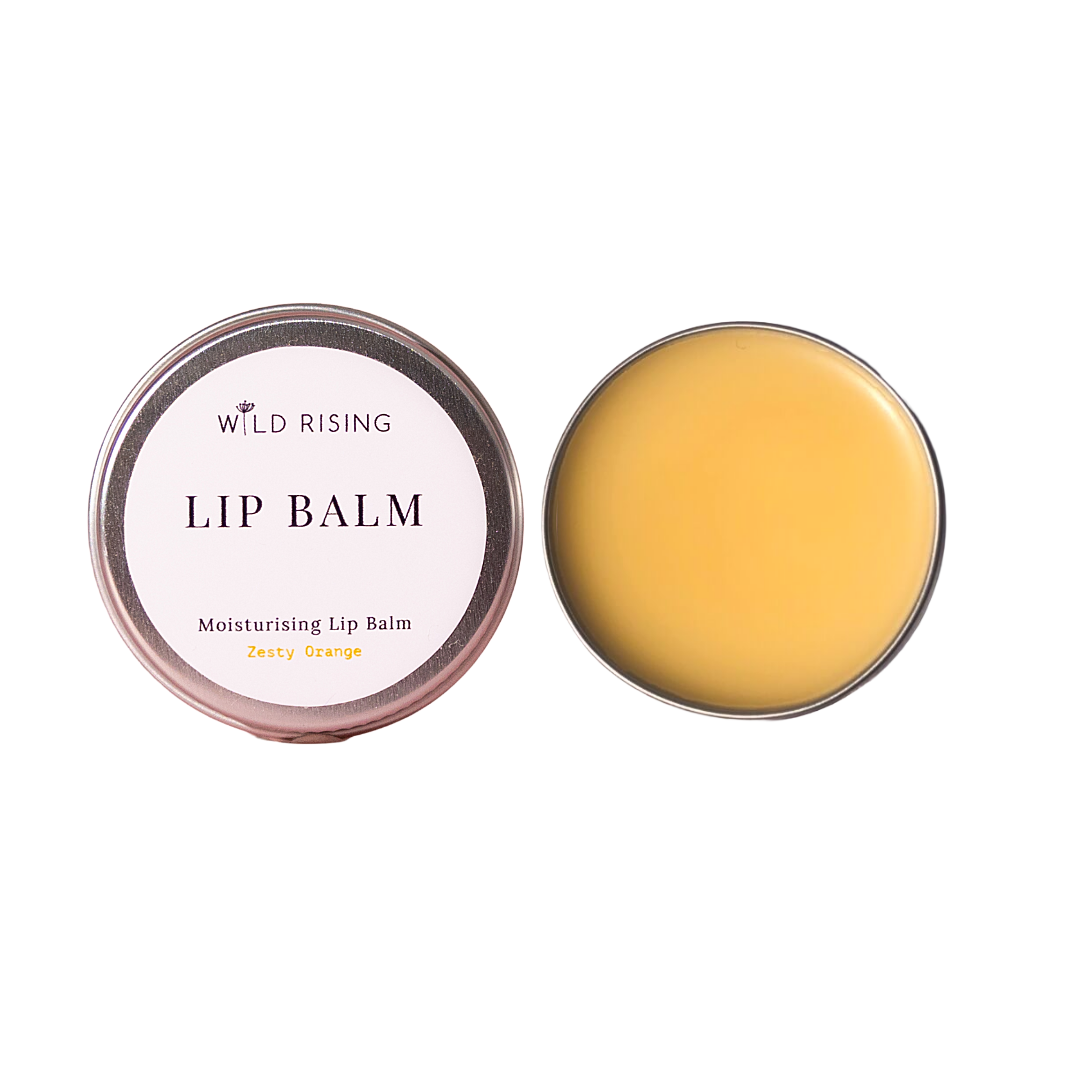 Two round metal tins of Wild Rising Lip Balm on a plain white background, one closed with a pale pink label reading 'LIP BALM Moisturising Lip Balm Zesty Orange' and one open showing the balm inside, which is a warm yellow-orange color.