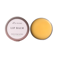 Two round metal tins of Wild Rising Lip Balm on a white background, one closed with a pale pink label and one open showing the yellow balm inside.