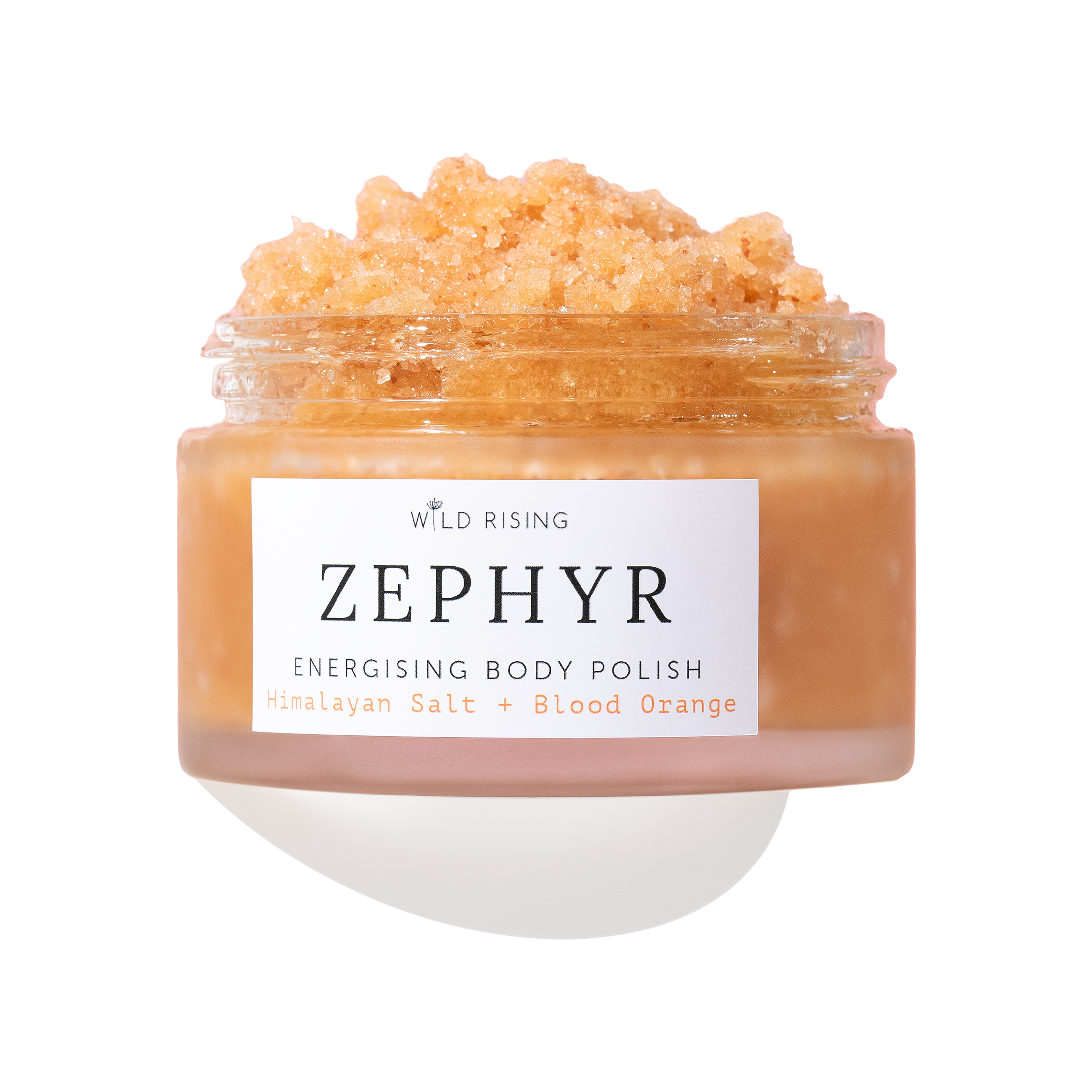 A clear jar of Wild Rising Zephyr Energising Body Polish filled with a peachy-orange granular scrub, shown on a white background with a soft shadow.