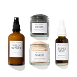 Four skincare products from Wild Rising arranged on a white background: a brown spray bottle labeled Wild Flower, a gray detox mask jar labeled Detox, a beige powder cleanser jar labeled Naked, and a dark seed oil bottle labeled Super Seed.