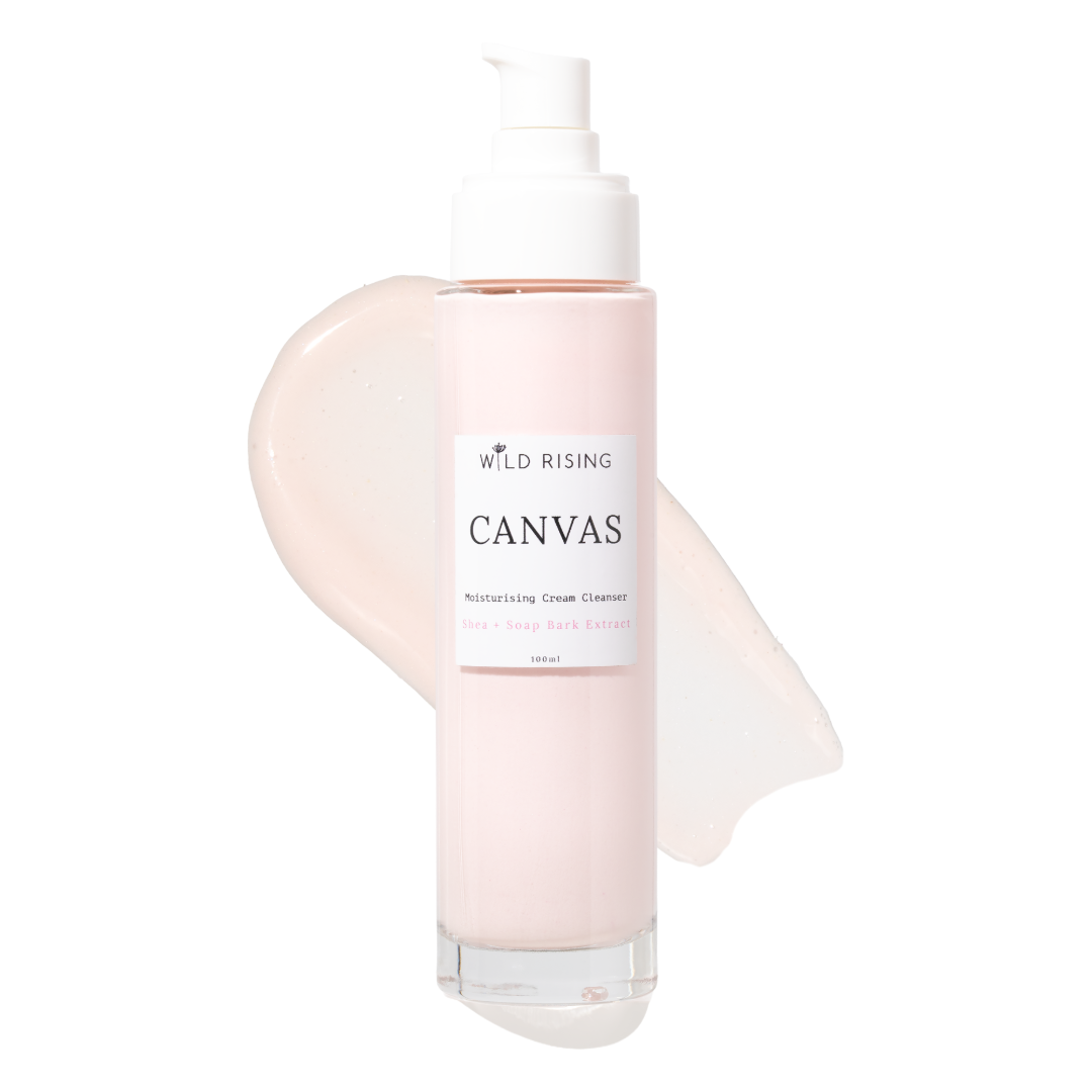 A bottle of Wild Rising Canvas Moisturizing Cream Cleanser with a white pump dispenser, set against a clean white background with a pale pink cream smear behind it.