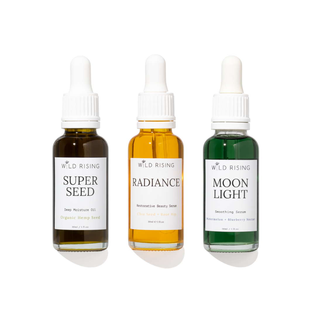 Three Wild Rising dropper bottles arranged side by side on a white background: Super Seed deep moisture oil in dark amber, Radiance restorative beauty serum in golden amber, and Moon Light smoothing serum in green.