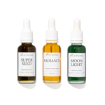 Three Wild Rising dropper bottles arranged side by side on a white background: Super Seed deep moisture oil in dark amber, Radiance restorative beauty serum in golden amber, and Moon Light smoothing serum in green.
