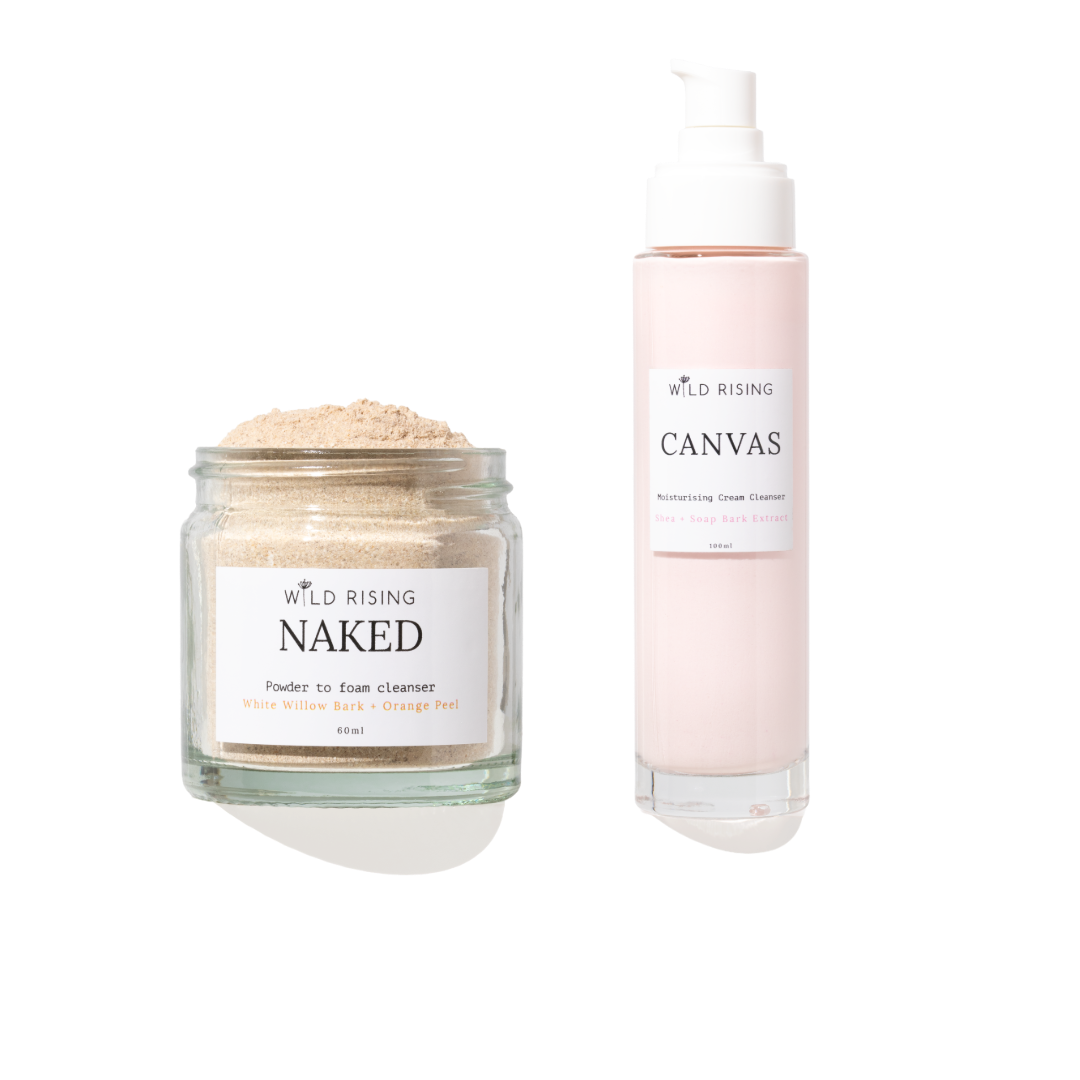 Two skincare products from Wild Rising on a white background: a clear glass jar of Naked Powder to Foam Cleaner with beige powder, and a pale pink pump bottle of Canvas Cream Cleaner.