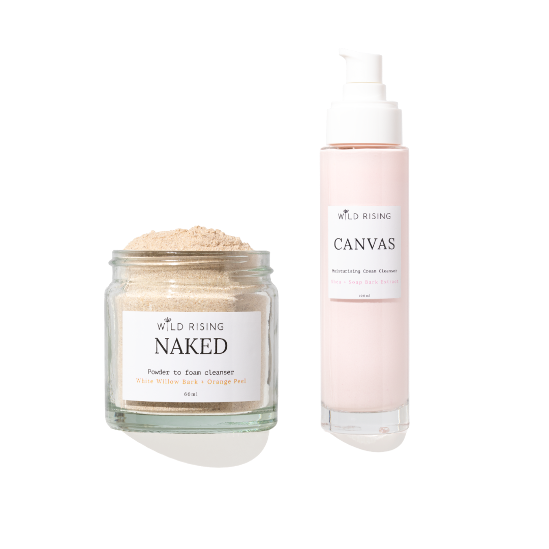 Two skincare products from Wild Rising on a white background: a clear glass jar of Naked Powder to Foam Cleaner with beige powder, and a pale pink pump bottle of Canvas Cream Cleaner.