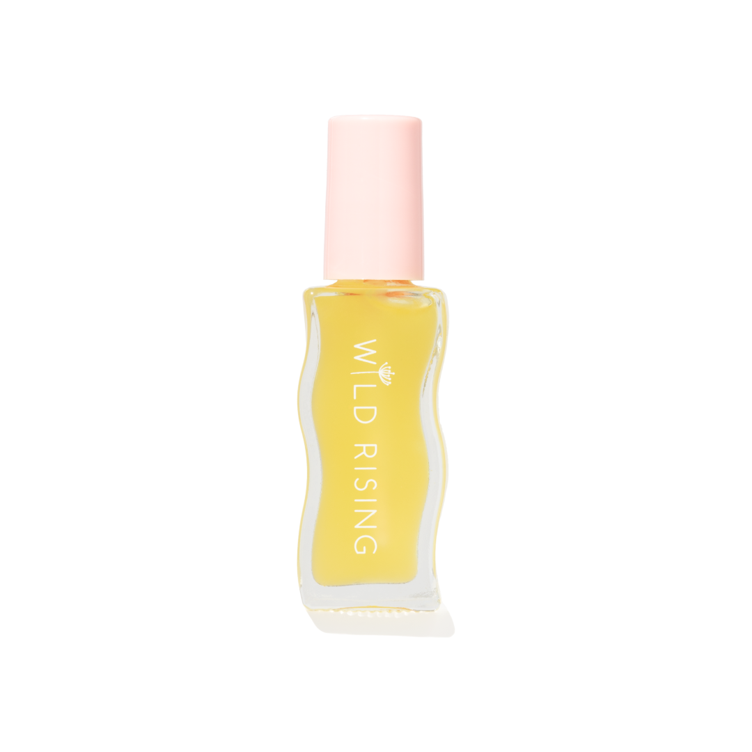 A small clear bottle filled with pale yellow liquid, featuring a light pink cap and vertical white text reading 'WILD RISING' on the front, centered on a plain white background.