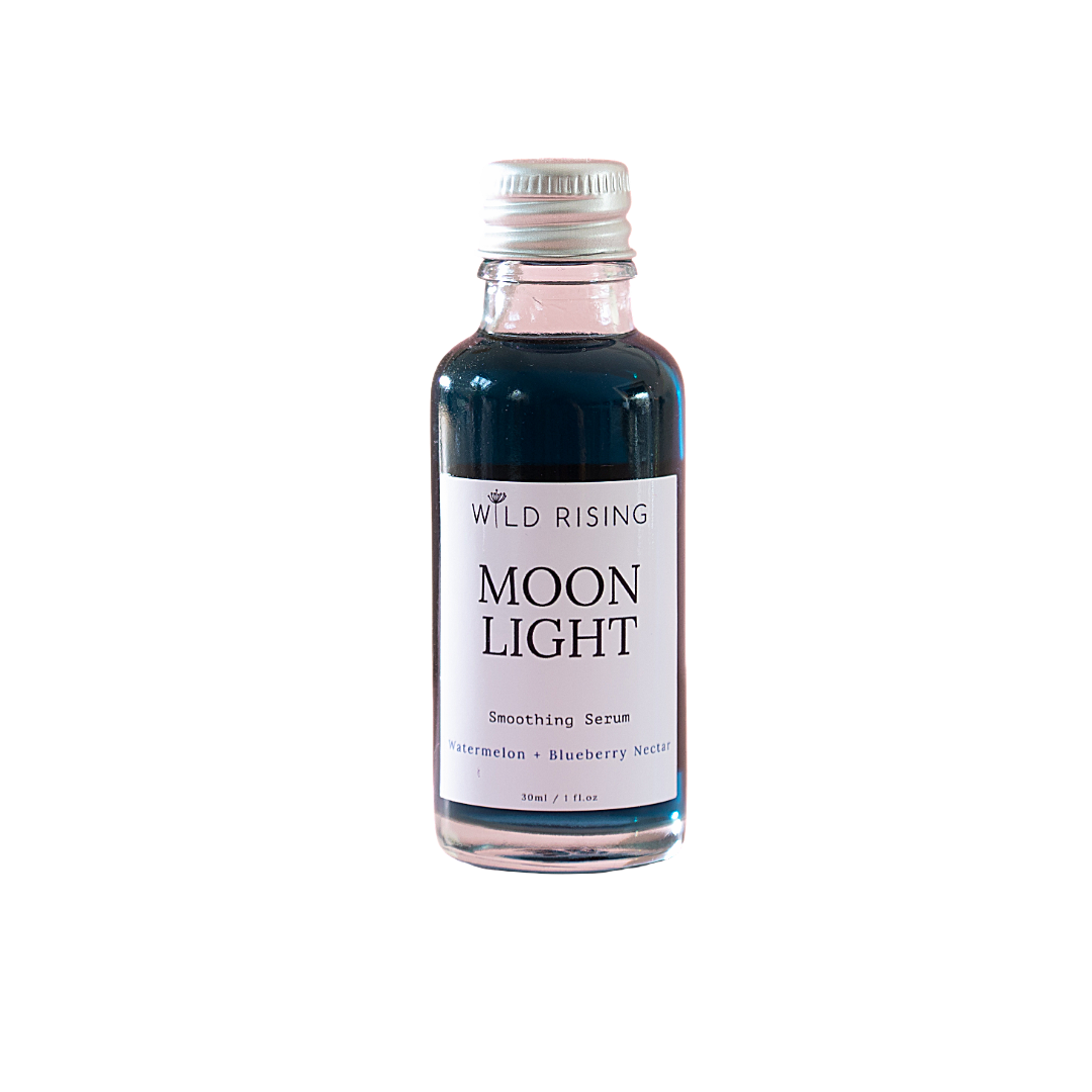 A small glass bottle of Wild Rising Moon Light Smoothing Serum with a silver cap and a white label, containing a dark blue liquid, set against a plain white background.