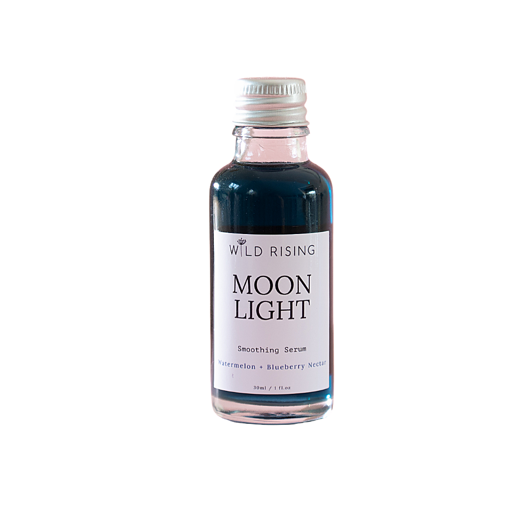 A small glass bottle of Wild Rising Moon Light Smoothing Serum with a silver cap and a white label, containing a dark blue liquid, set against a plain white background.