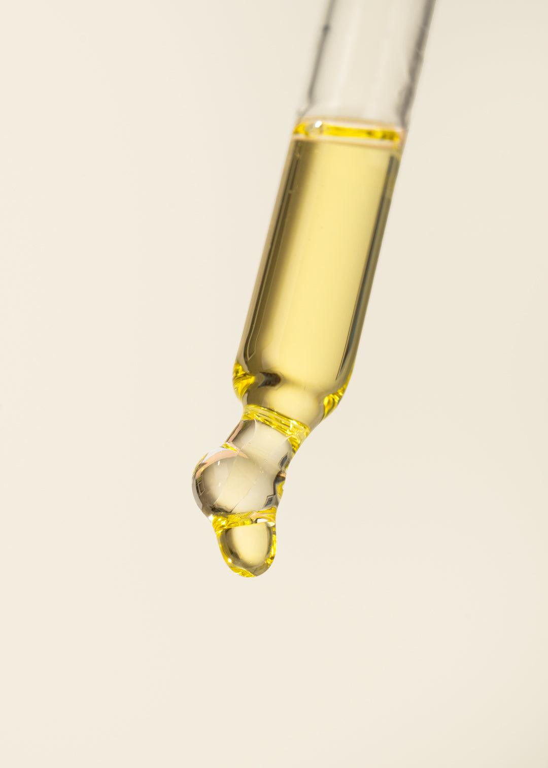 Glass dropper with yellow liquid on a beige background