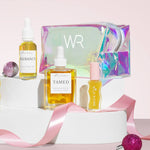 hair oil, face oil and lip oil stood up in front of a holographic bag