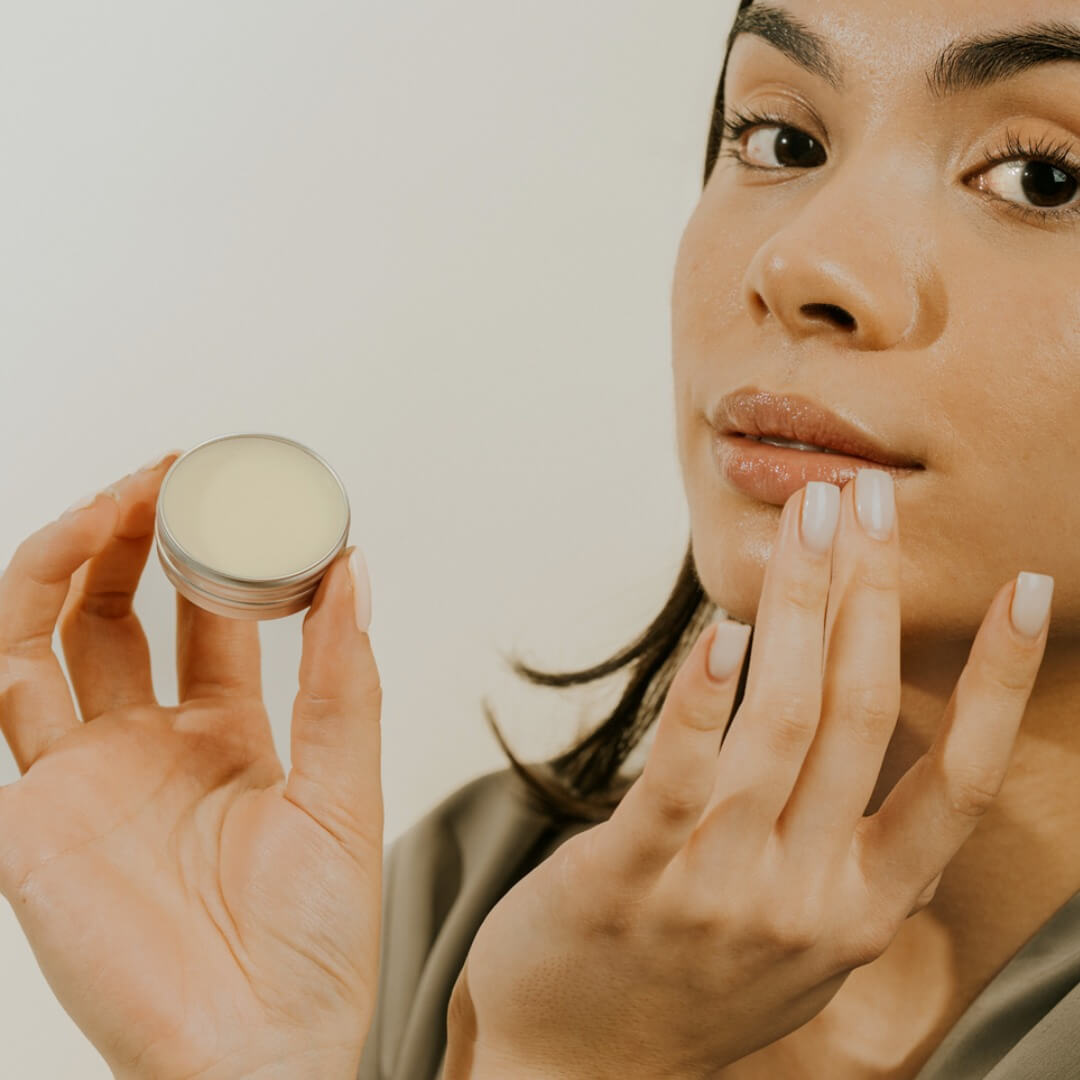 Woman applying lip balm to her lips with a neutral background