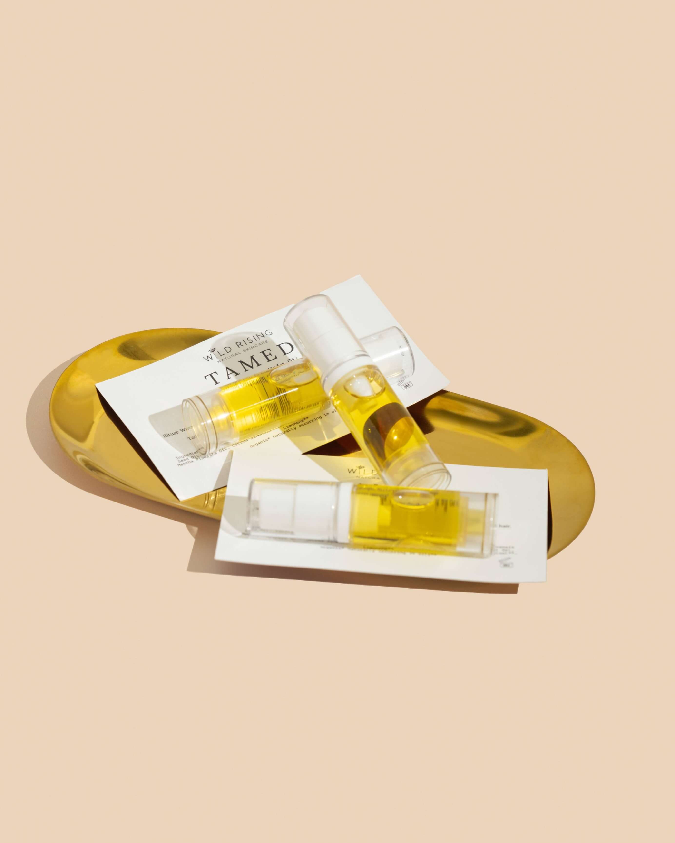 three mini bottles of hair oil on a gold tray with a cream background