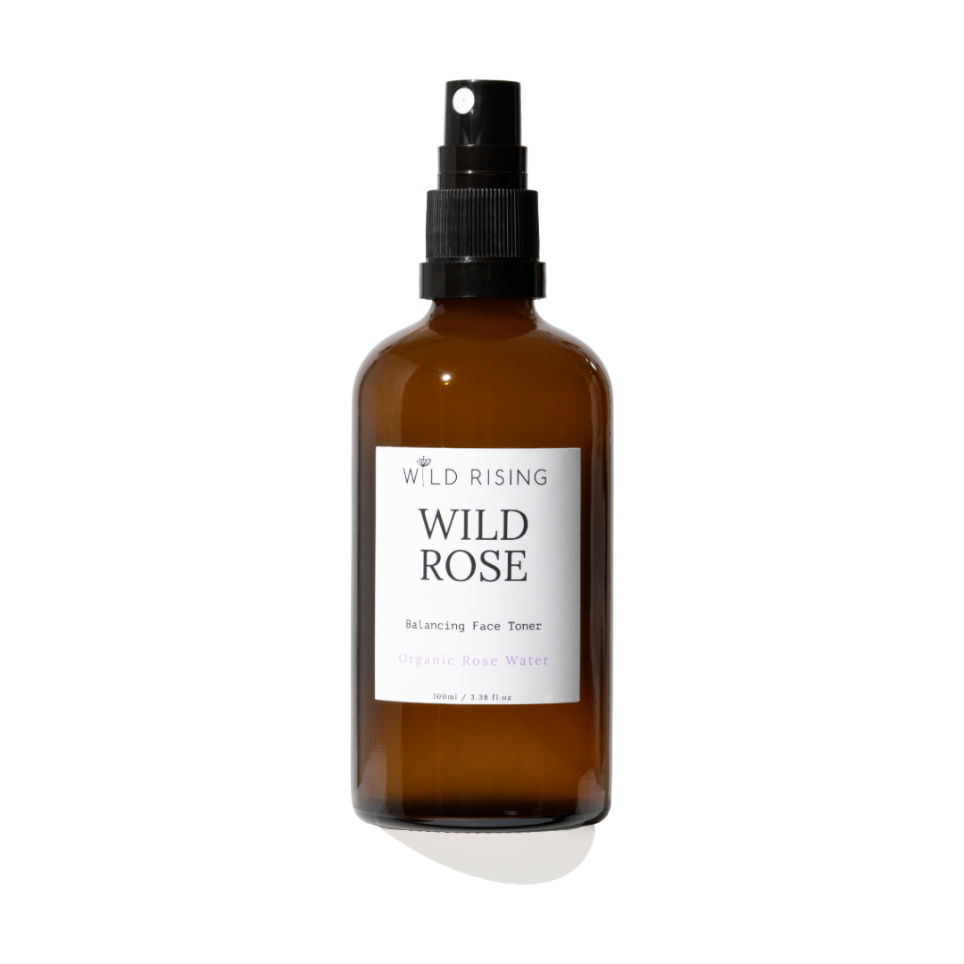 An amber glass face toner spray bottle with a black spray nozzle and a white label reading 'WILD RISING WILD ROSE'.