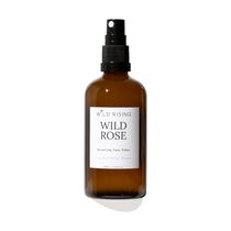 An amber glass face toner spray bottle with a black spray nozzle and a white label reading 'WILD RISING WILD ROSE'.