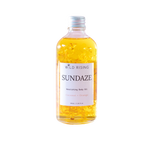 A bottle of Wild Rising Sundaze Coconut + Orange nourishing body oil, filled with golden yellow oil and suspended calendula pieces, on a solid white background.