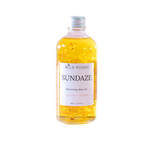 A bottle of Wild Rising Sundaze Coconut + Orange nourishing body oil, filled with golden yellow oil and suspended calendula pieces, on a solid white background.