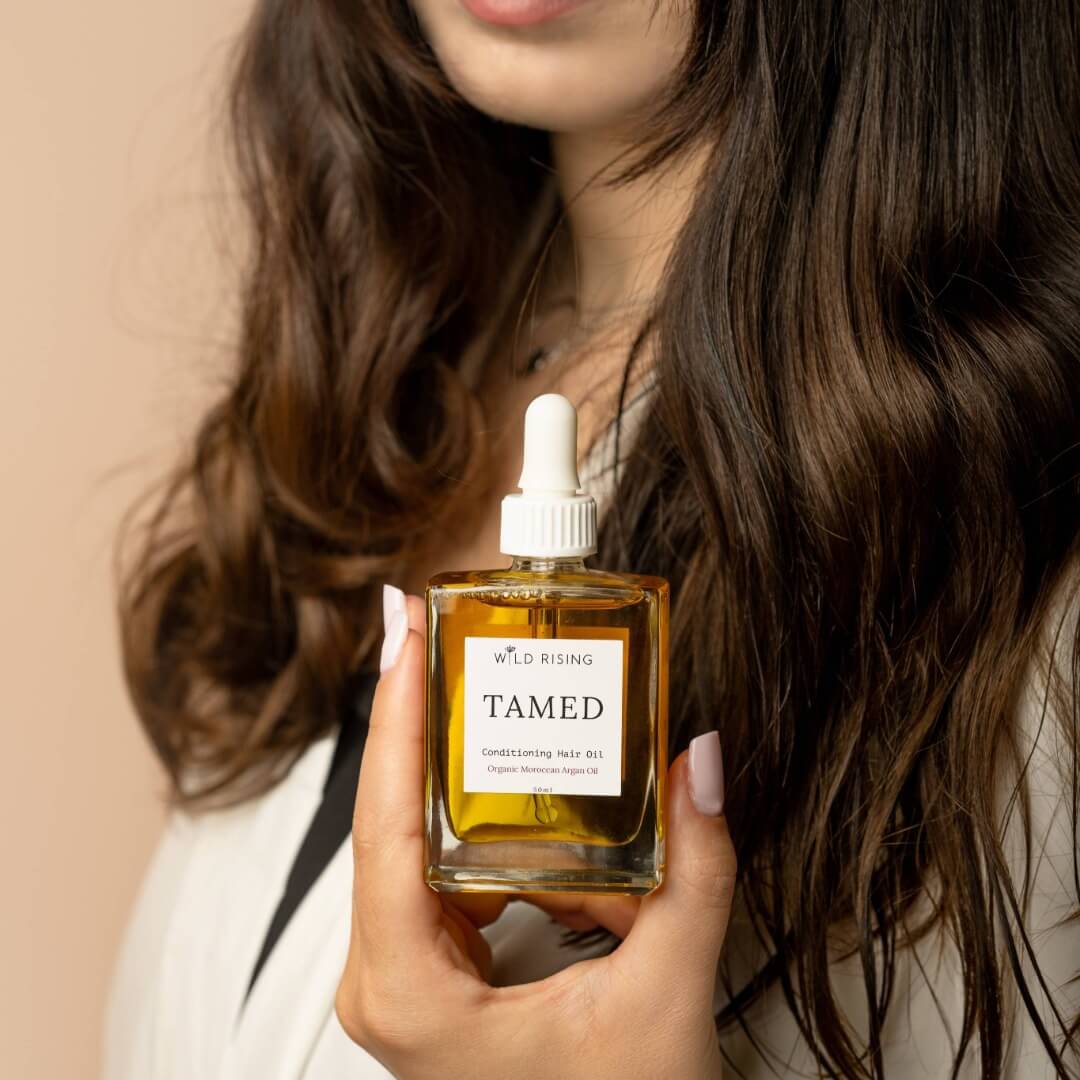brunette holding a square hair oil bottle