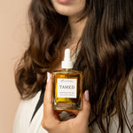 brunette holding a square hair oil bottle