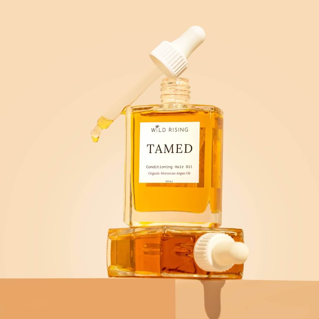 two square bottles, one laid down and the other resting on top with hair oil in