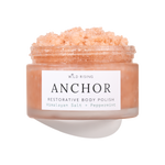 A jar of Wild Rising Anchor Restorative Body Polish, filled with a peach-colored crystalline scrub, shown against a clean white background with a soft shadow.