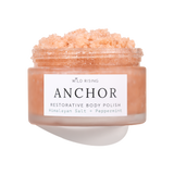 A jar of Wild Rising Anchor Restorative Body Polish, filled with a peach-colored crystalline scrub, shown against a clean white background with a soft shadow.