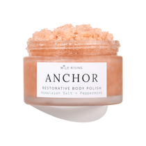 A jar of Wild Rising Anchor Restorative Body Polish, filled with a peach-colored crystalline scrub, shown against a clean white background with a soft shadow.
