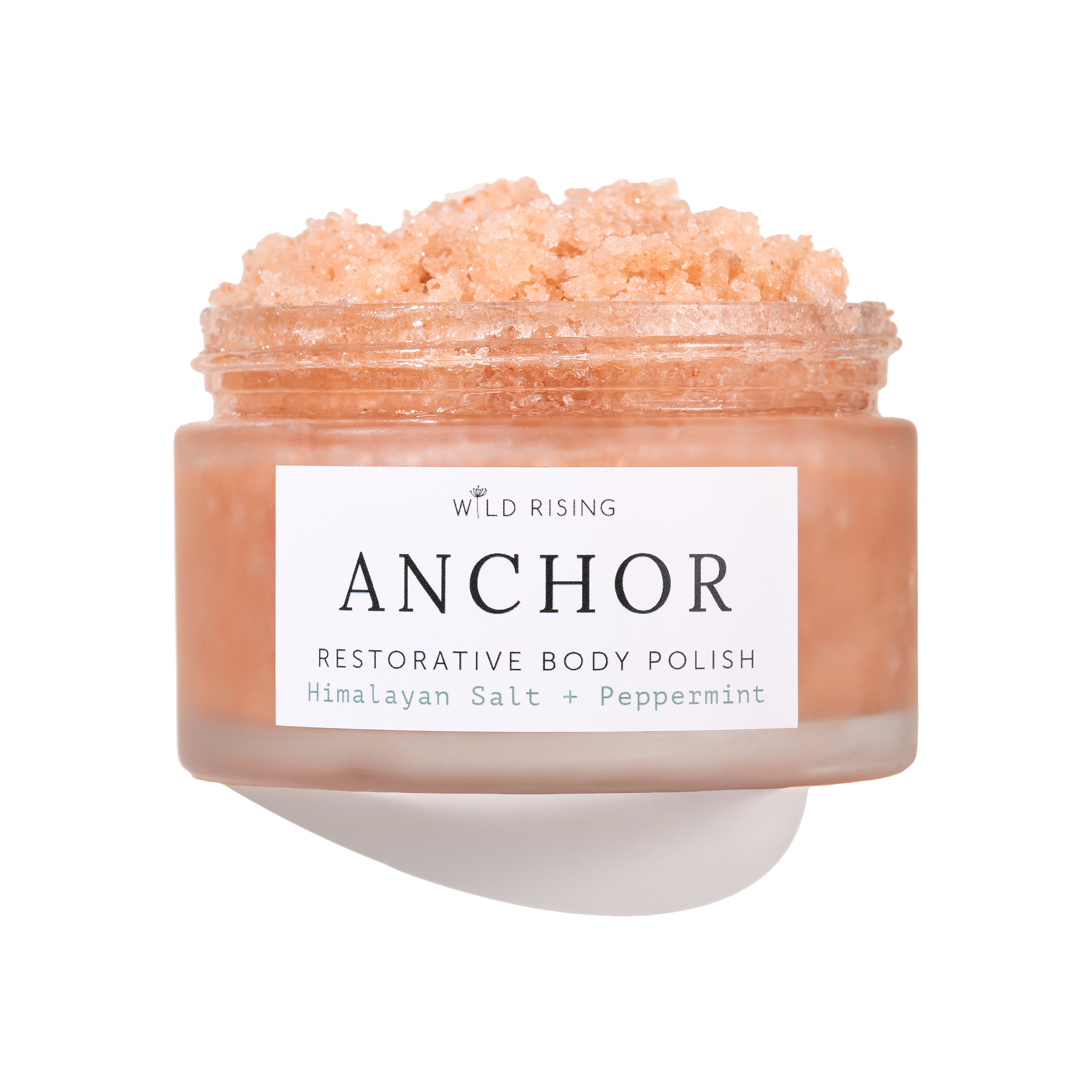 A jar of Wild Rising Anchor Restorative Body Polish, filled with a peach-colored crystalline scrub, shown against a clean white background with a soft shadow.