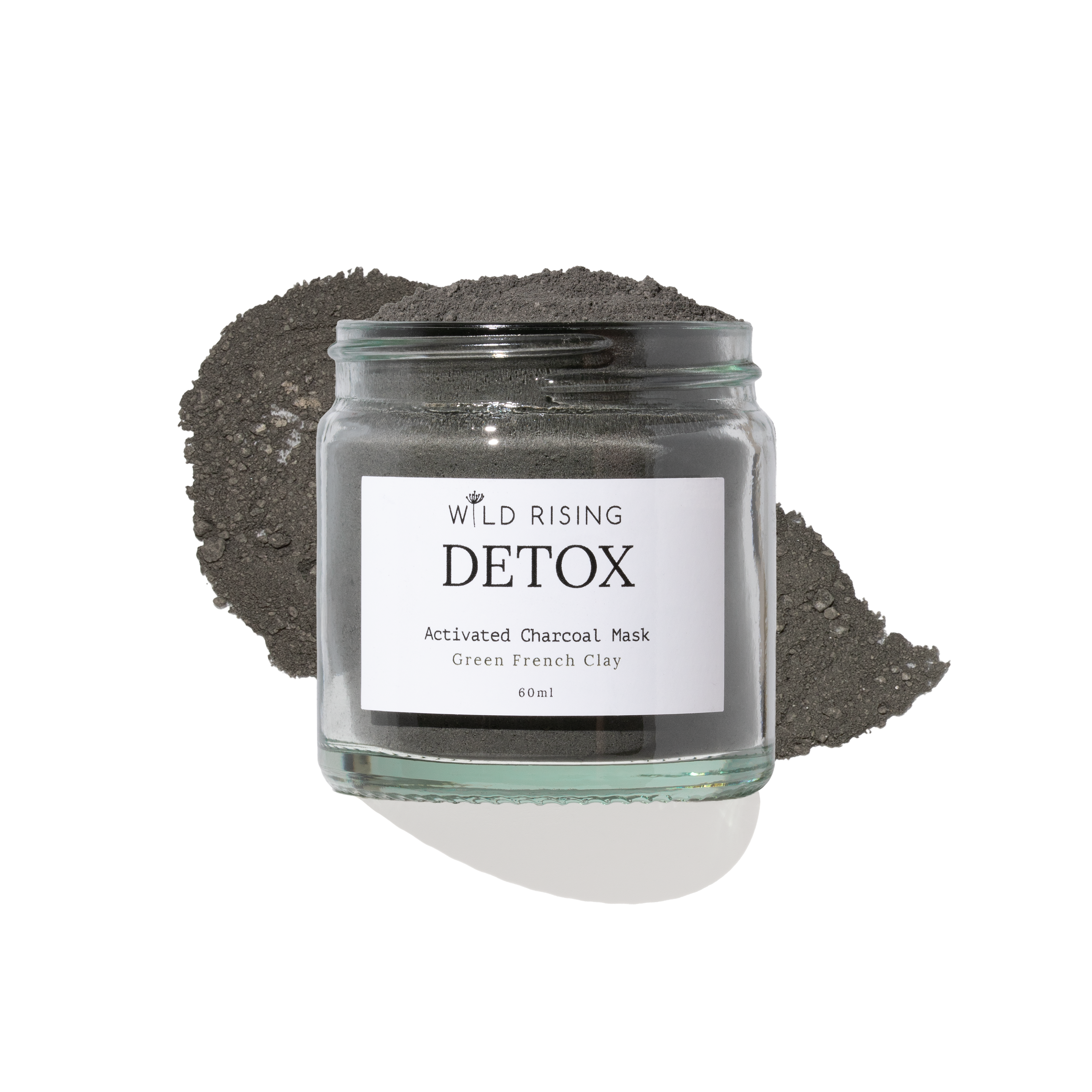 A glass jar of Wild Rising Detox Activated Charcoal Mask, filled with dark green French clay powder and topped with a small pile of the same charcoal mask, set against a clean white background.