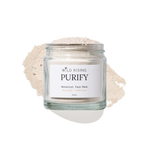 A clear glass jar labeled 'WILD RISING PURIFY Botanical Face Mask' filled with a light beige powder, set against a white background with a matching powder spill behind it.