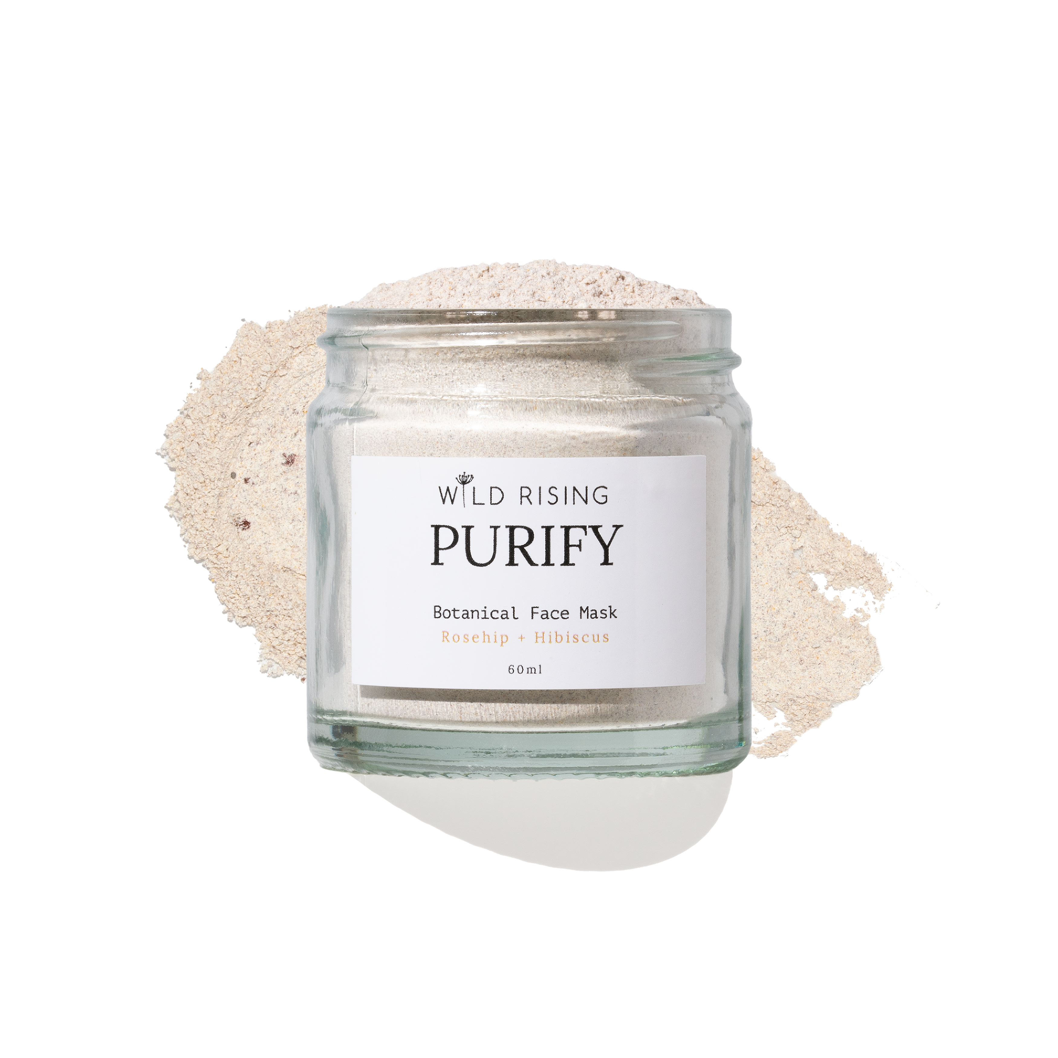 A clear glass jar labeled 'WILD RISING PURIFY Botanical Face Mask' filled with a light beige powder, set against a white background with a matching powder spill behind it.