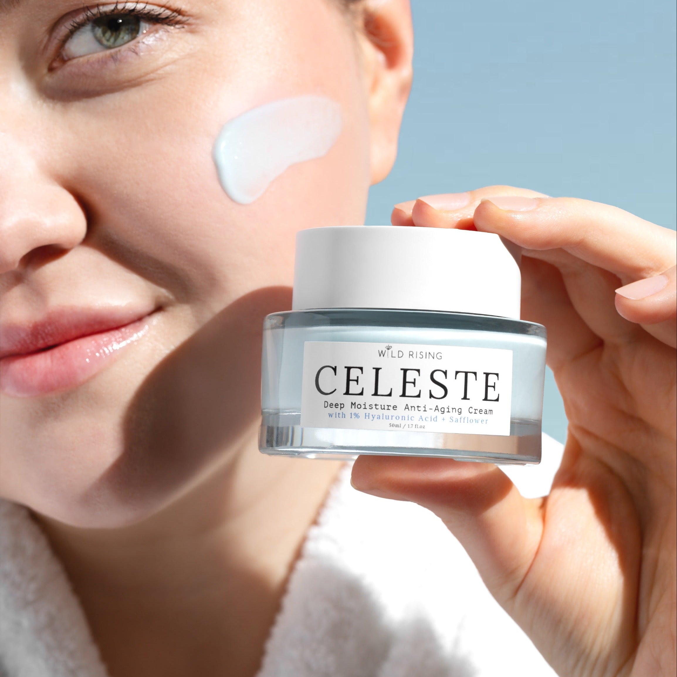 Person applying cream to face with Celeste jar in hand against a clear sky.
