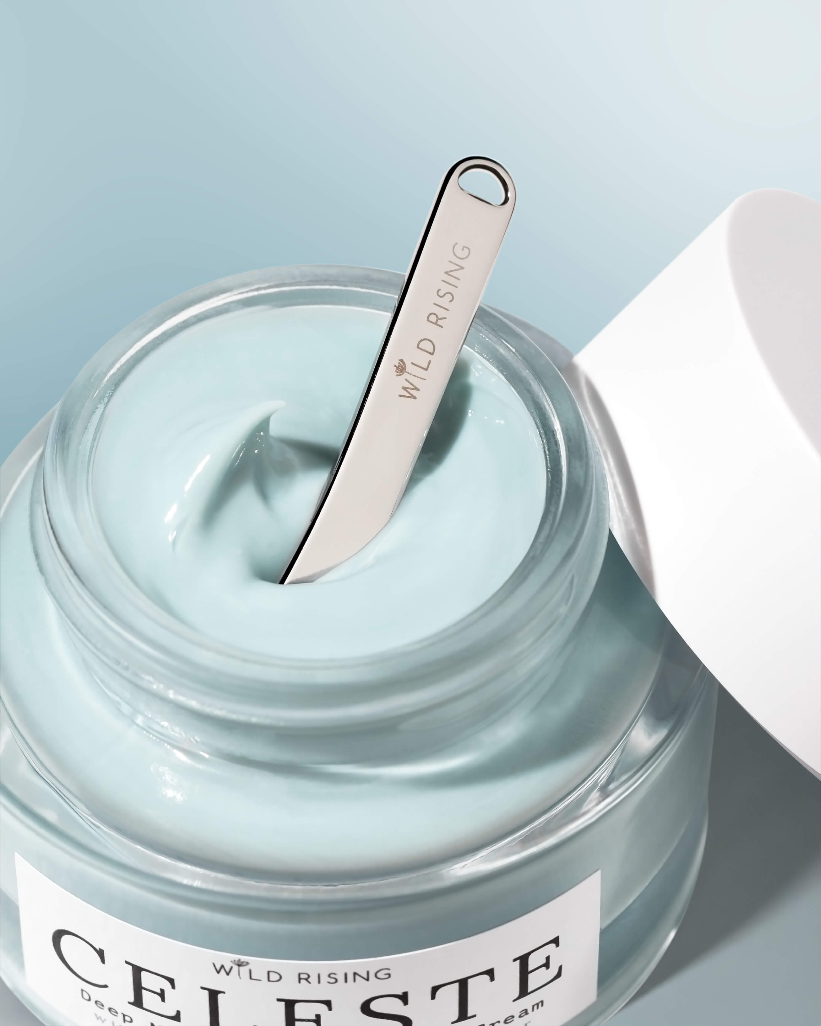 skincare spatula sitting inside a jar of blue face cream